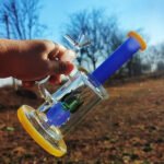 colorful glass bong with blue neck and yellow base held outdoors