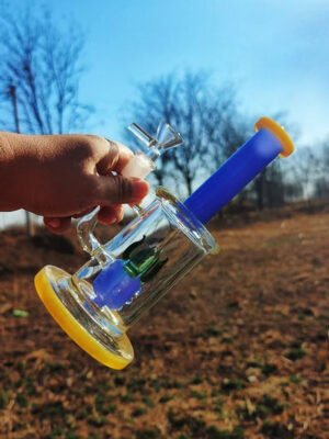 colorful glass bong with blue neck and yellow base held outdoors