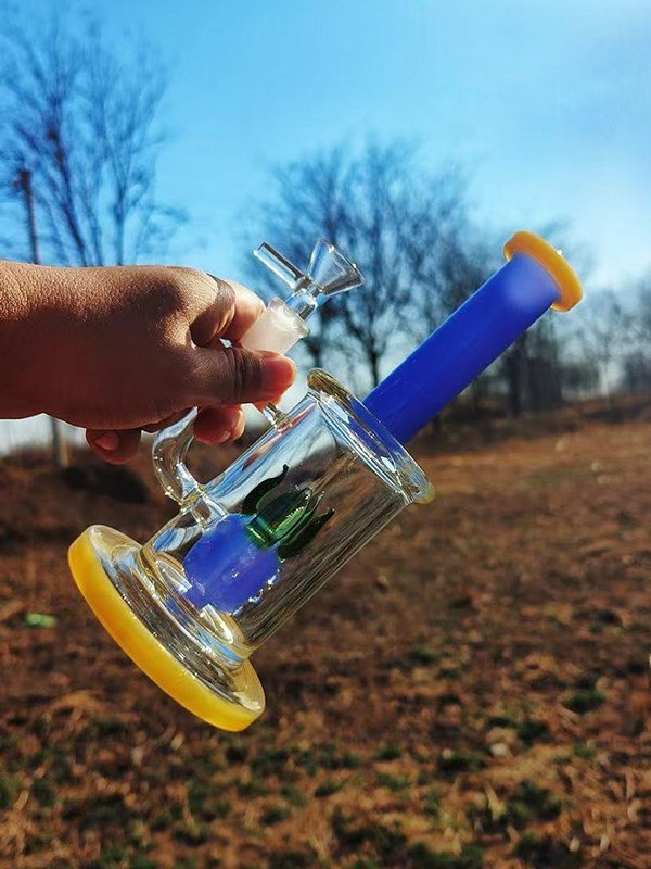 colorful glass bong with blue neck and yellow base held outdoors